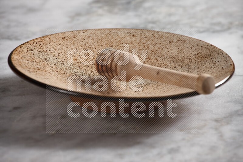 Multicolored pottery plate with wooden honey dipper in it on grey marble background