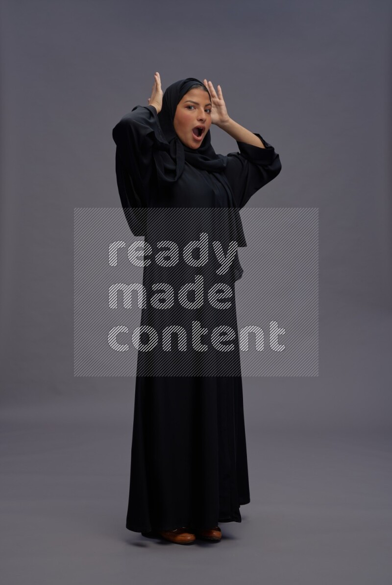 Saudi woman wearing Abaya standing hands behind head on gray background