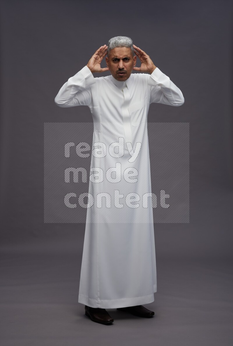 Saudi man wearing thob standing hands behind head on gray background