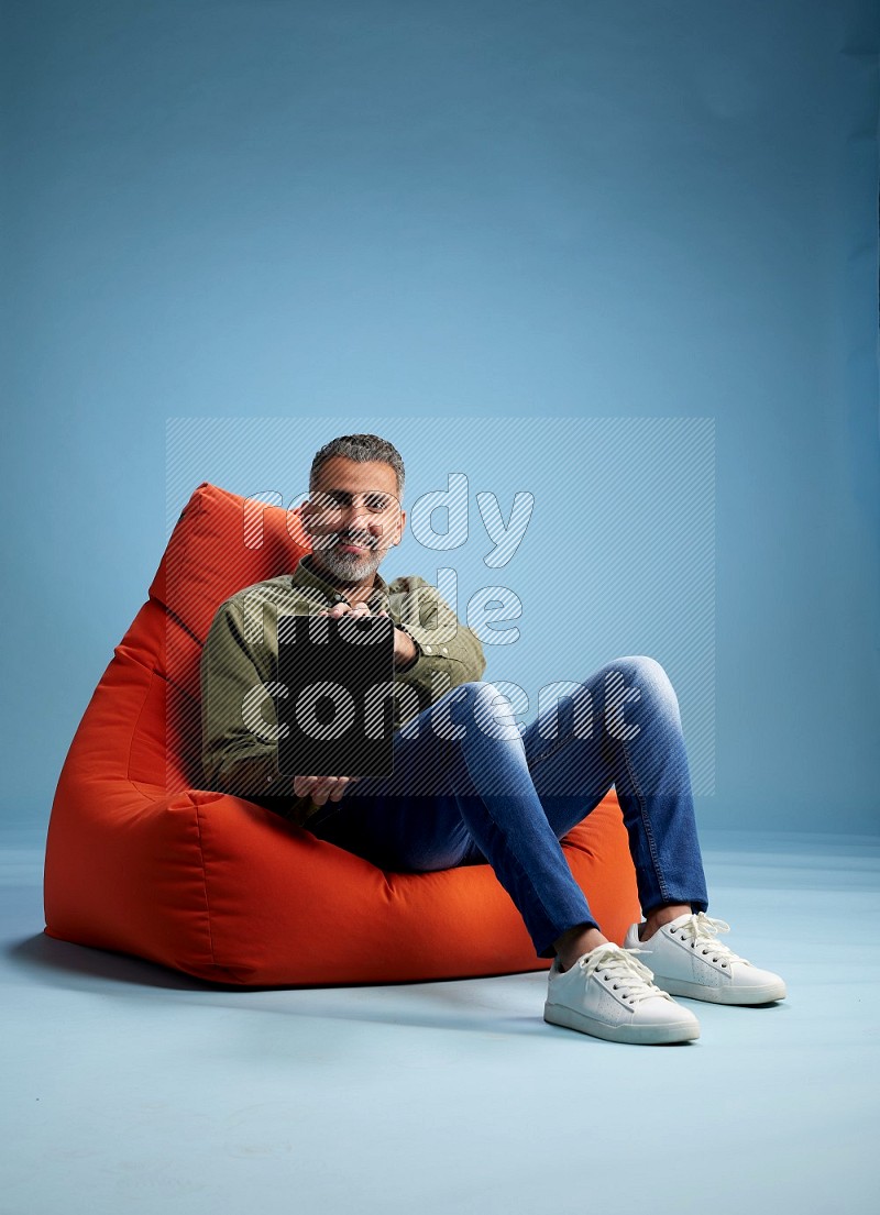 A man sitting on an orange beanbag and working on tablet