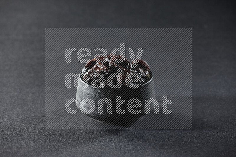 وعاء فخاري أسود ممتلئ بالبرقوق المجفف على خلفية سوداء