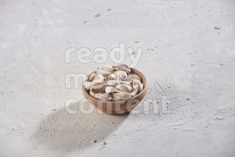 A wooden bowl full of garlic cloves on a white flooring