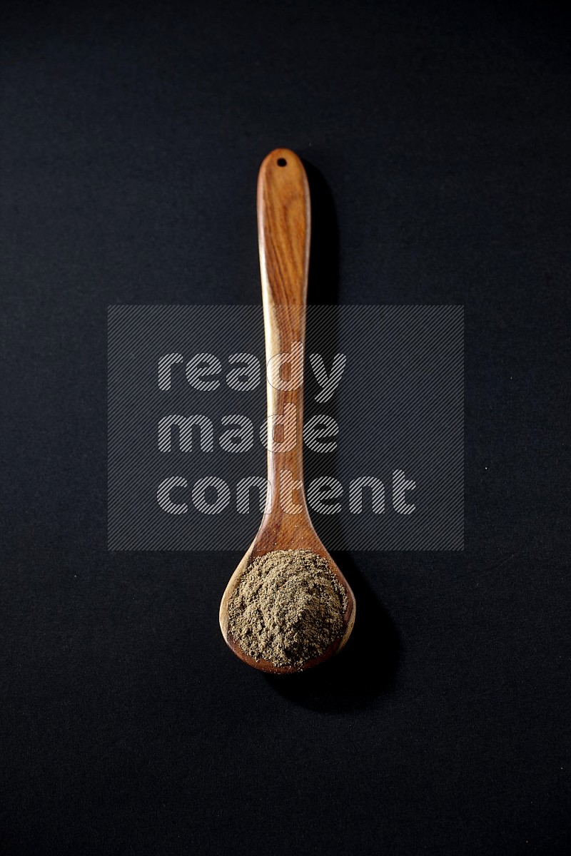 A wooden ladle full of cardamom powder on black flooring