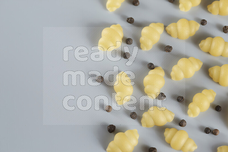 Raw pasta with different ingredients such as cherry tomatoes, garlic, onions, red chilis, black pepper, white pepper, bay laurel leaves, rosemary, cardamom and mushrooms on light blue background