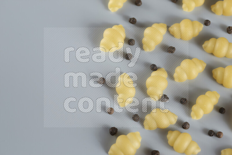 Raw pasta with different ingredients such as cherry tomatoes, garlic, onions, red chilis, black pepper, white pepper, bay laurel leaves, rosemary, cardamom and mushrooms on light blue background
