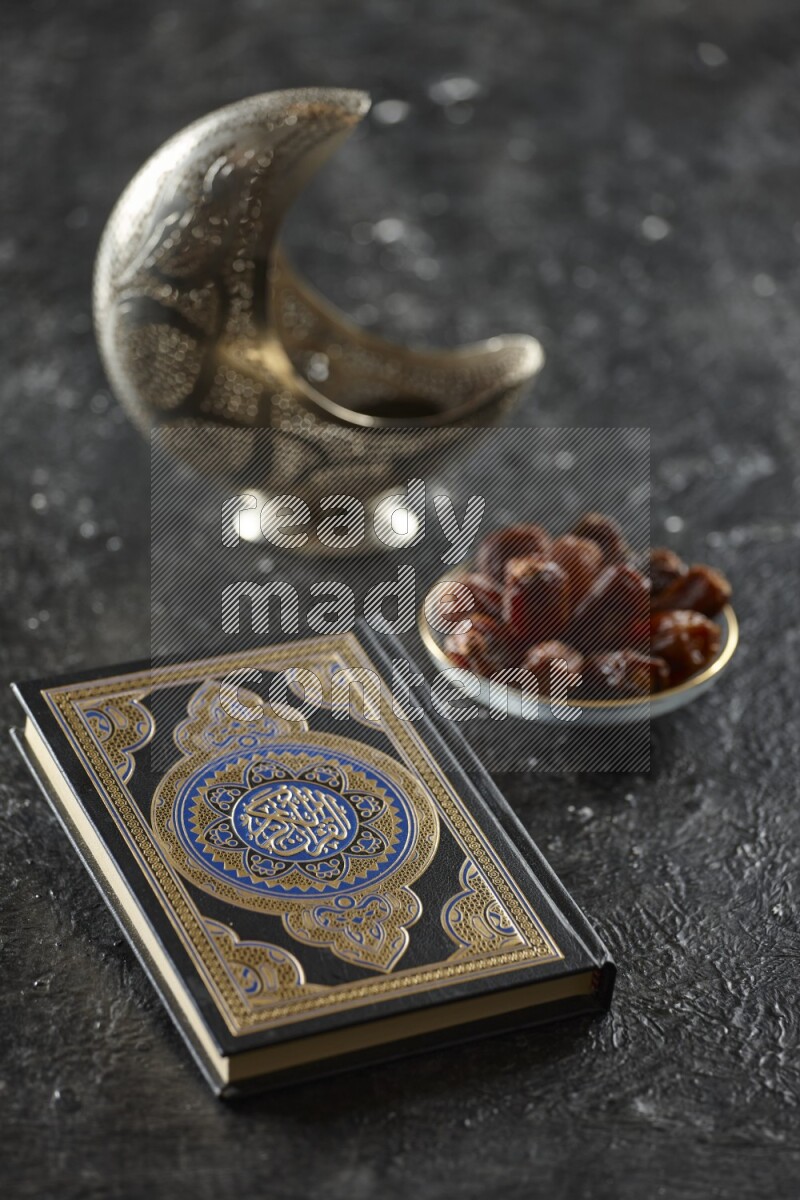 A silver lantern with different drinks, dates, nuts, prayer beads and quran on textured black background