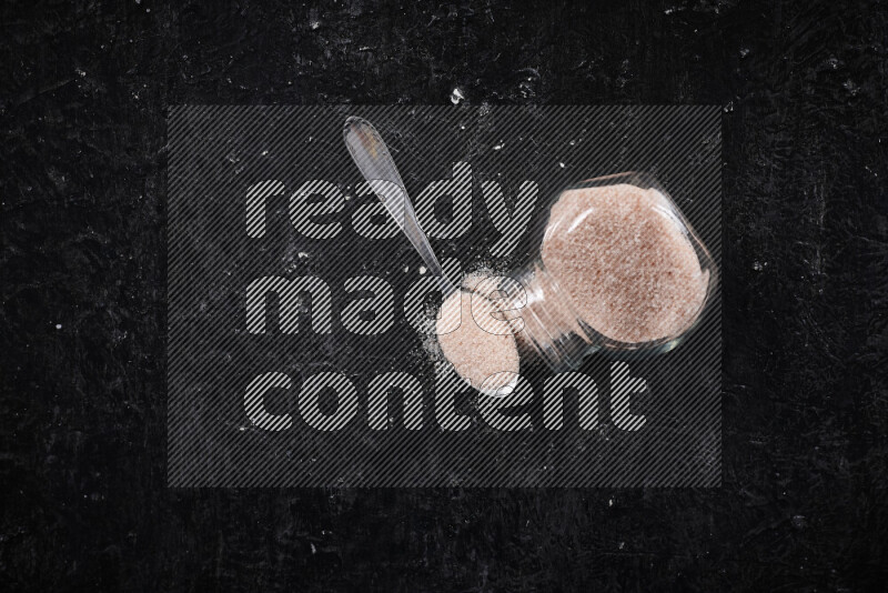 A glass jar full of fine himalayan salt on black background