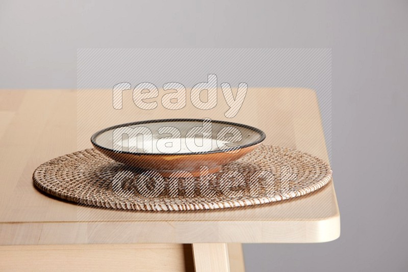 multi-colored pottery Plate placed on a big light colored straw placemat on the edge of wooden table