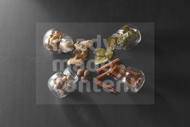 أوراق الغار وزنجبيل مجفف وقرفة وجوزة الطيب في أوعية زجاجية علي خلفية سوداء