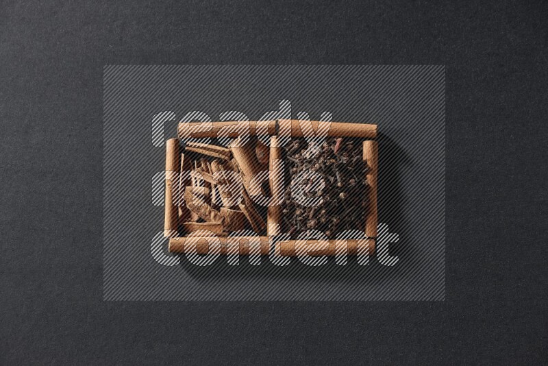 مربعان من أعواد القرفة ممتلئان بالقرنفل وقطع القرفة علي خلفية سوداء