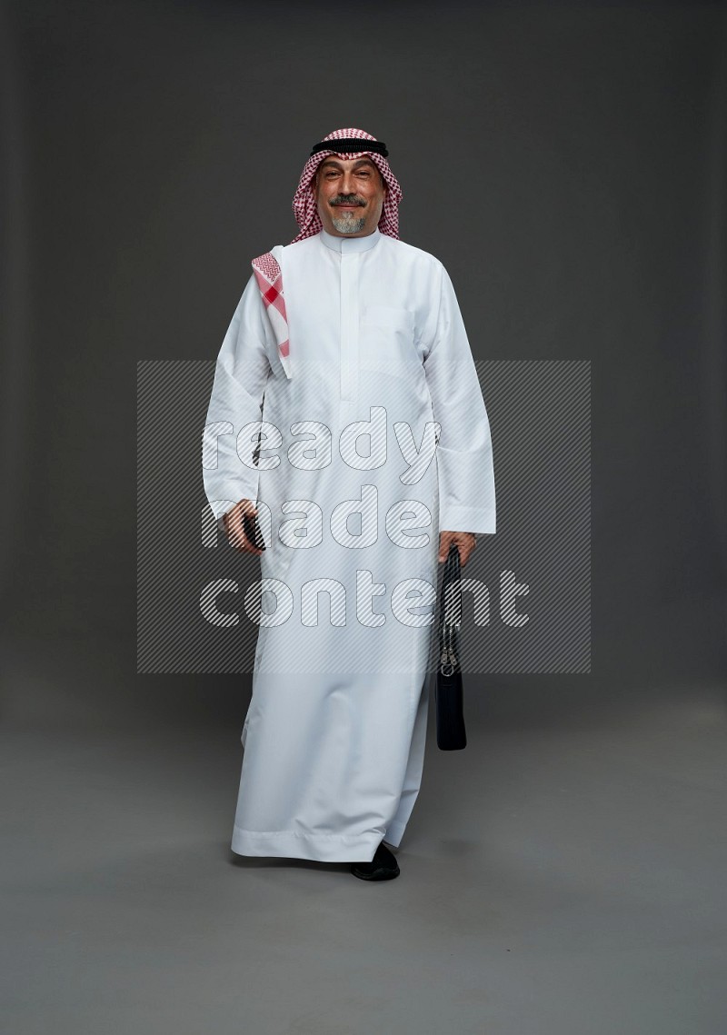 Saudi man with shomag Standing holding bag and phone on gray background