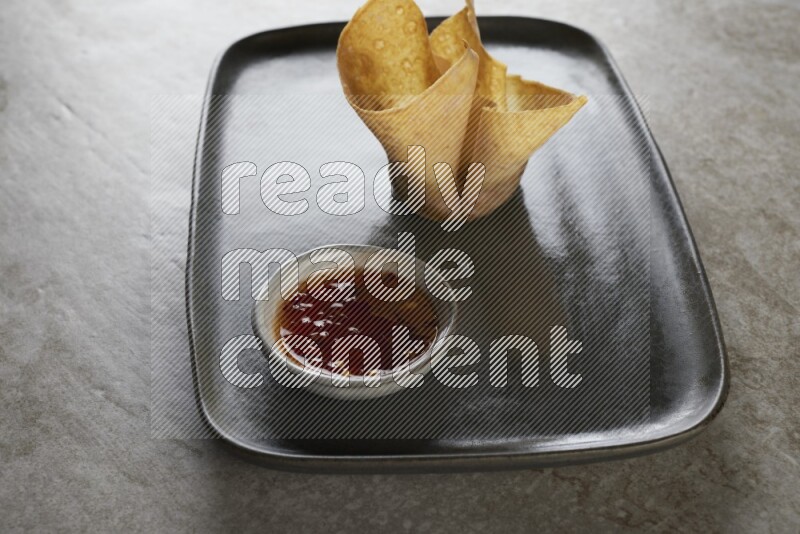 wonton cups with soy sauce ramkin on rectangle dark grey ceramic plate on grey textured counter top