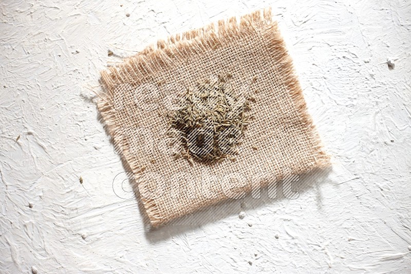 Cumin seeds on a burlap piece on a textured white flooring