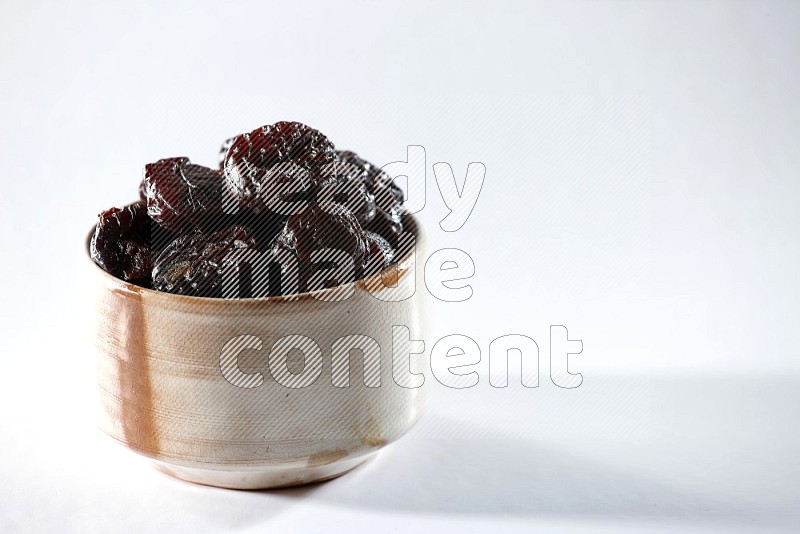 A beige ceramic bowl full of dried plums on a white background in different angles