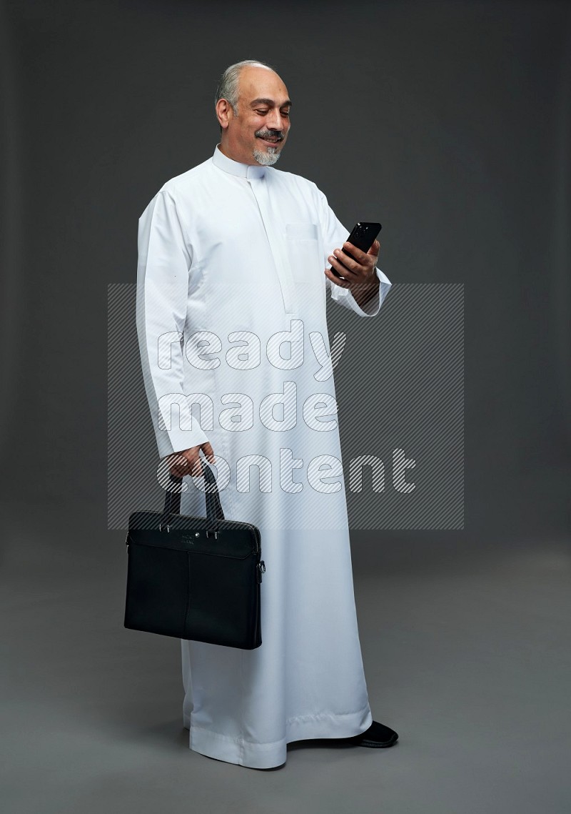 Saudi man without shomag Standing holding bag and phone on gray background