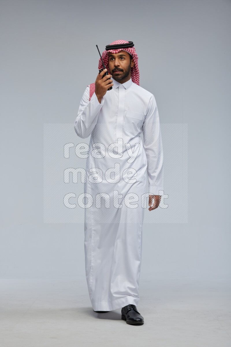 Saudi man Wearing Thob and shomag standing holding walkie-talkie on Gray background