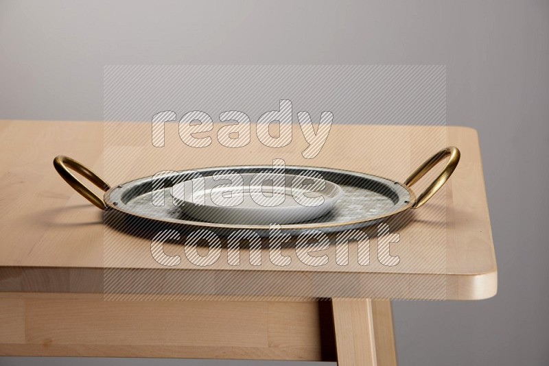 white plate placed on a rounded stainless steel tray with golden handels on the edge of wooden table