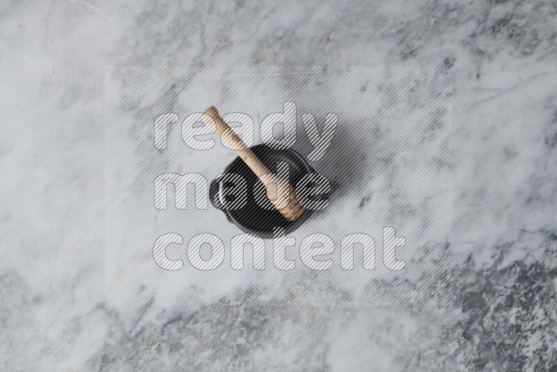 Black pottery bowl with wooden honey dipper in it on grey marble background
