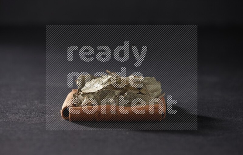 أربعة من أعواد القرفة مكونة شكل مربع بداخلها أوراق الغار علي خلفية سوداء