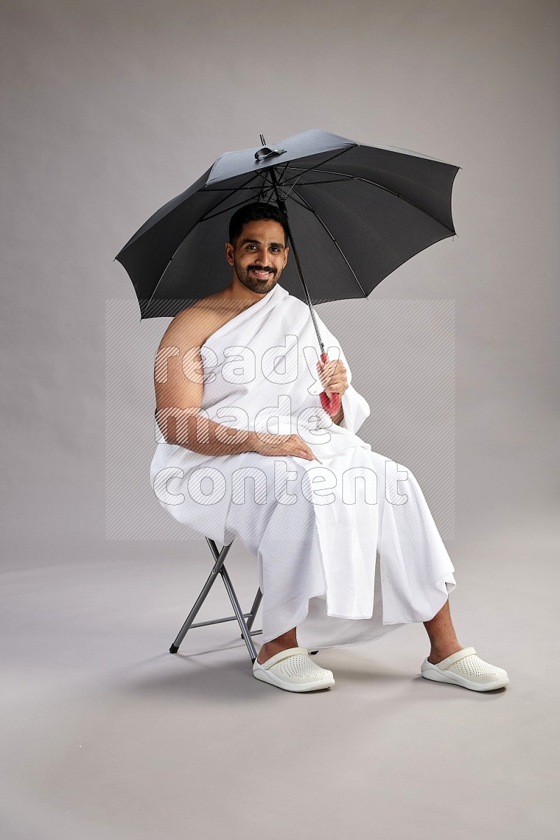 A man wearing Ehram with face mask Standing holding umbrella on gray background