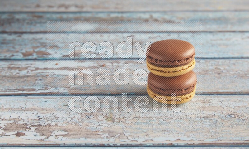 45º Shot of two Yellow and Brown Chai Latte macarons on light blue wooden background
