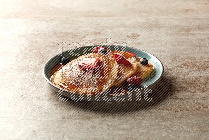 Three stacked mixed berries pancakes in a blue plate on beige background