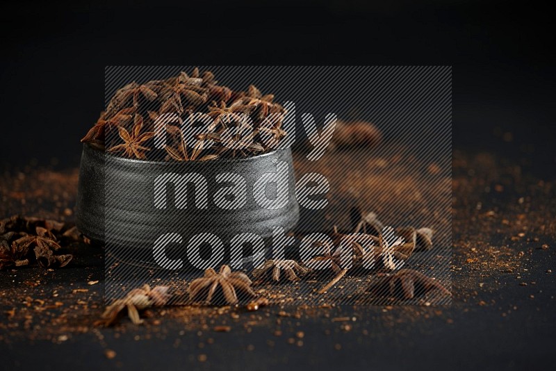 Star Anise in a black bowl with sprinkled anise on black flooring