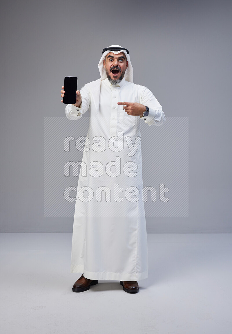 رجل سعودي يرتدي ثوب وشماغ ابيض يحمل جوال