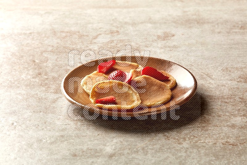 Five stacked strawberry mini pancakes in a brown plate on beige background