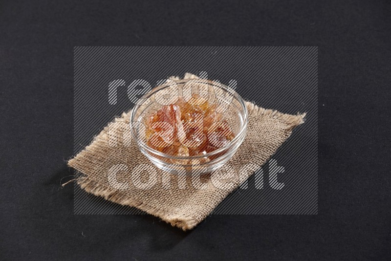 A glass bowl full of gum arabic on a burlap piece on black flooring