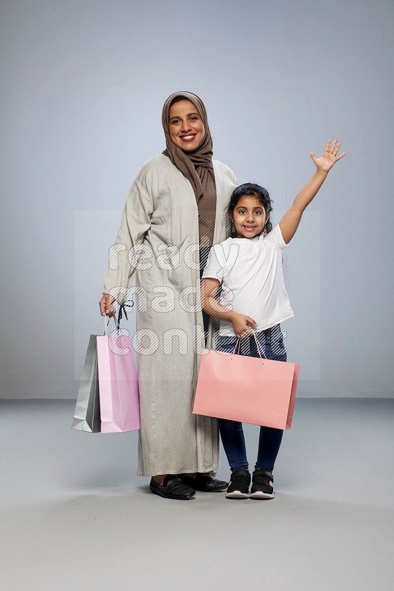 Mom and daughter holding shopping bags on gray background