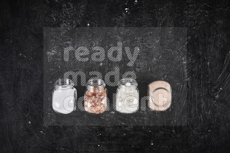 4 glass jars filled with table salt, coarse sea salt, fine himalayan salt and coarse himalayan salt on black background