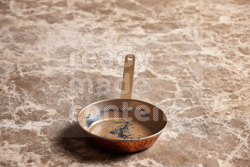 A small copper pan on beige marble background