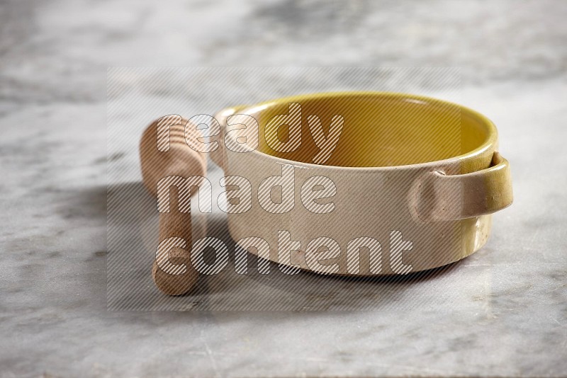 Multicolored Pottery bowl with wooden honey handle on the side with grey marble flooring, 15 degree angle