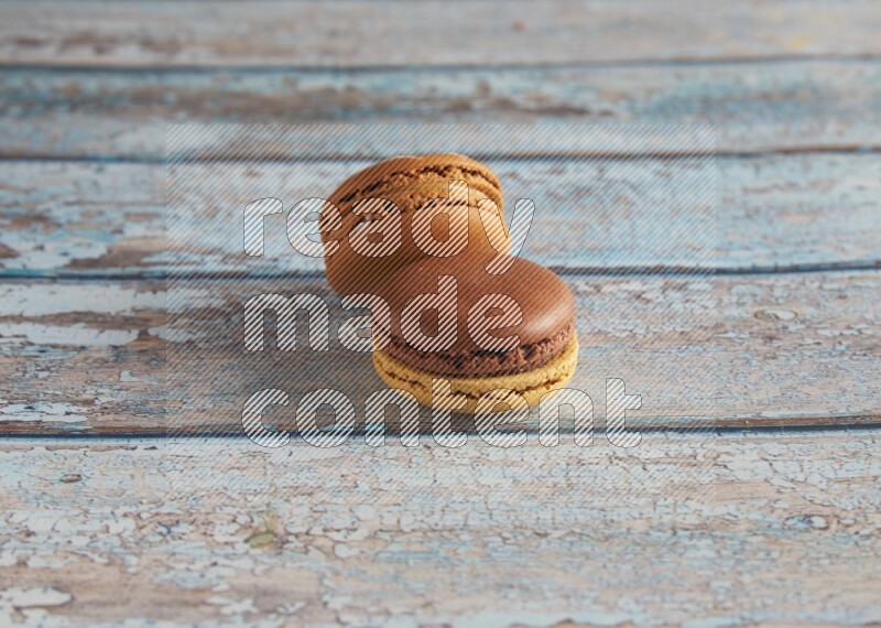 45º Shot of of two assorted Brown Irish Cream, and Yellow, and Brown Chai Latte macarons  on light blue background