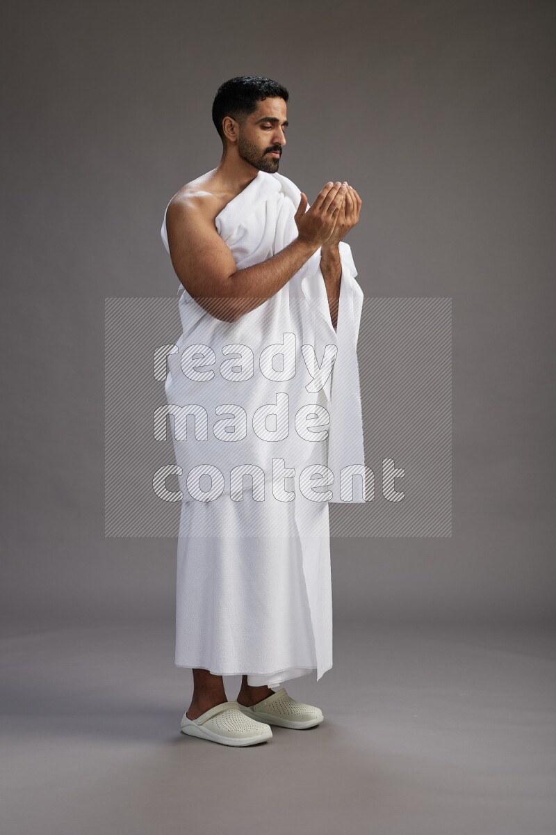 A man wearing Ehram Standing performing dua'a on gray background