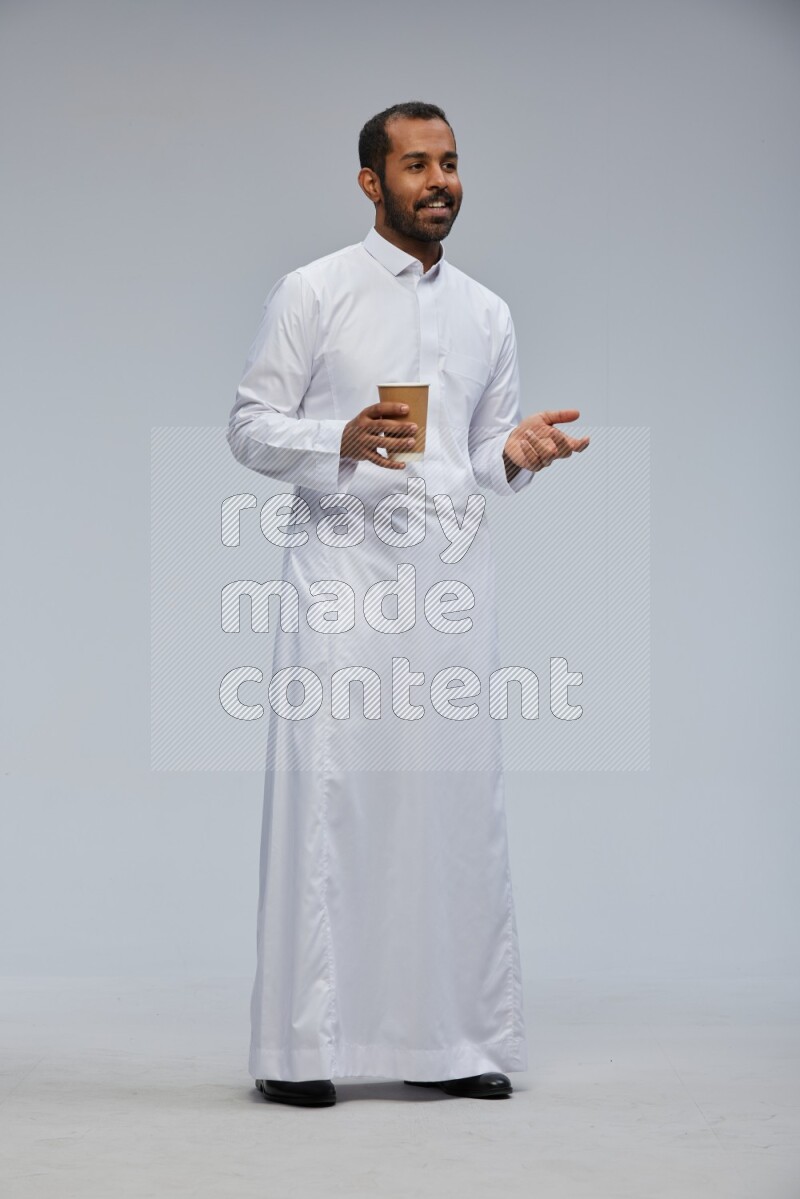 Saudi man wearing thob standing holding paper cup on gray background