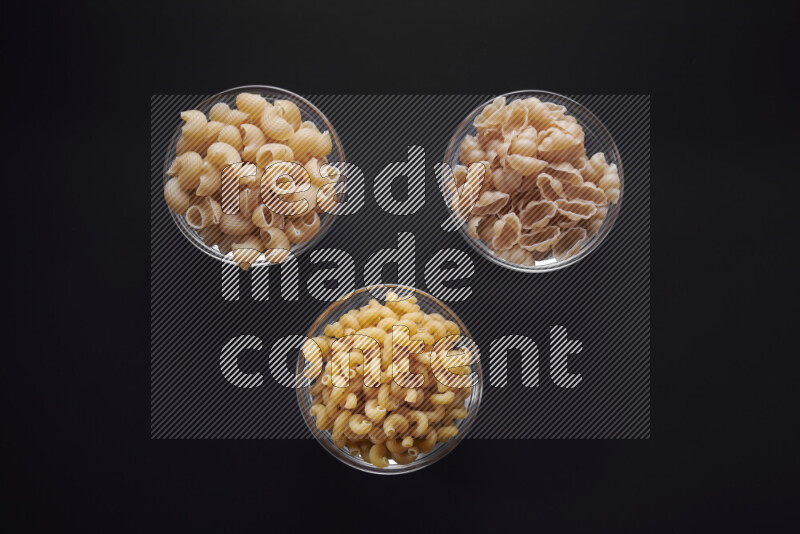 Different pasta types in glass bowls on black background