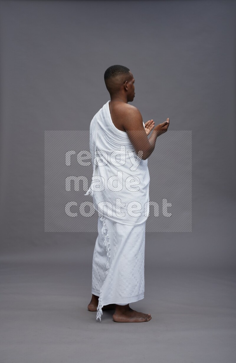 A man wearing Ehram Standing dua'a on gray background