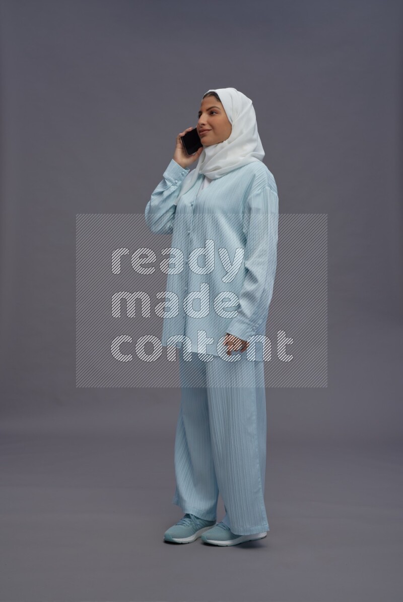 Saudi woman wearing hijab clothes standing talking on phone on gray background