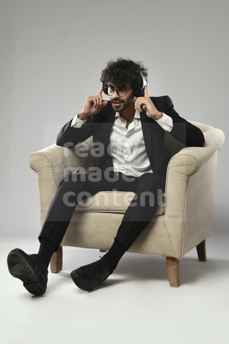 رجل يرتدي ملابس رسمية يجلس علي كرسي و يضع سماعات رأس علي خلفية بيضاء