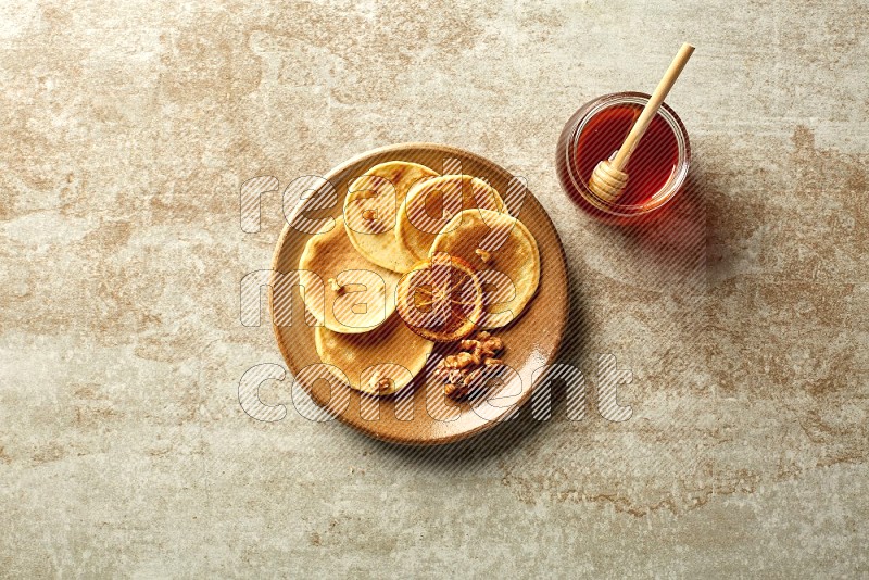 Five stacked dried orange mini pancakes in a brown plate on beige background