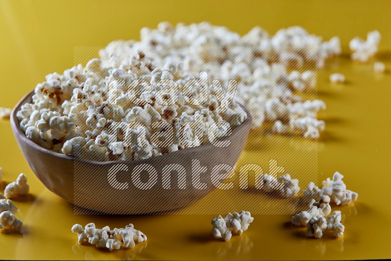 A brown pottery bowl full of popcorn with popcorn beside it on a yellow background in different angles
