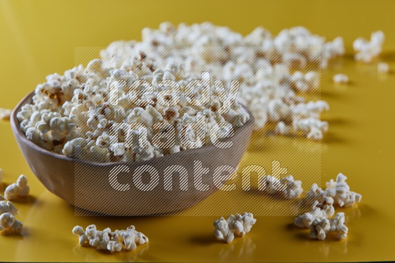 A brown pottery bowl full of popcorn with popcorn beside it on a yellow background in different angles
