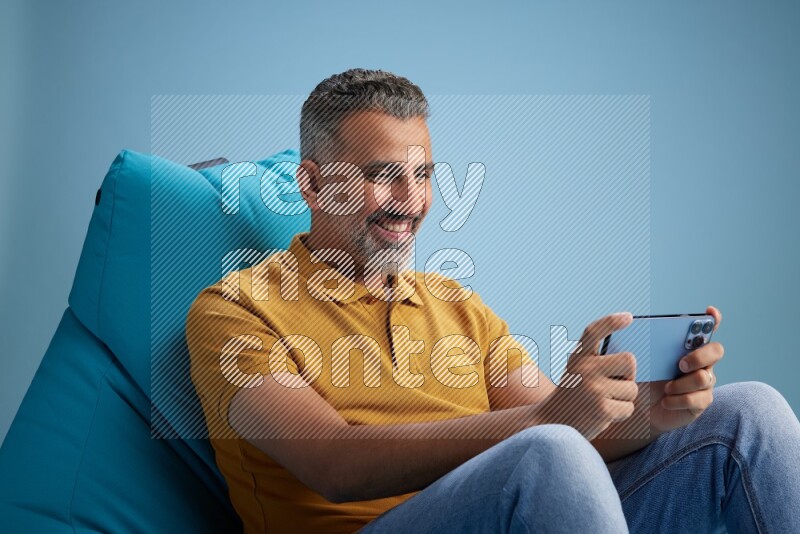 A man sitting on a blue beanbag and playing on phone
