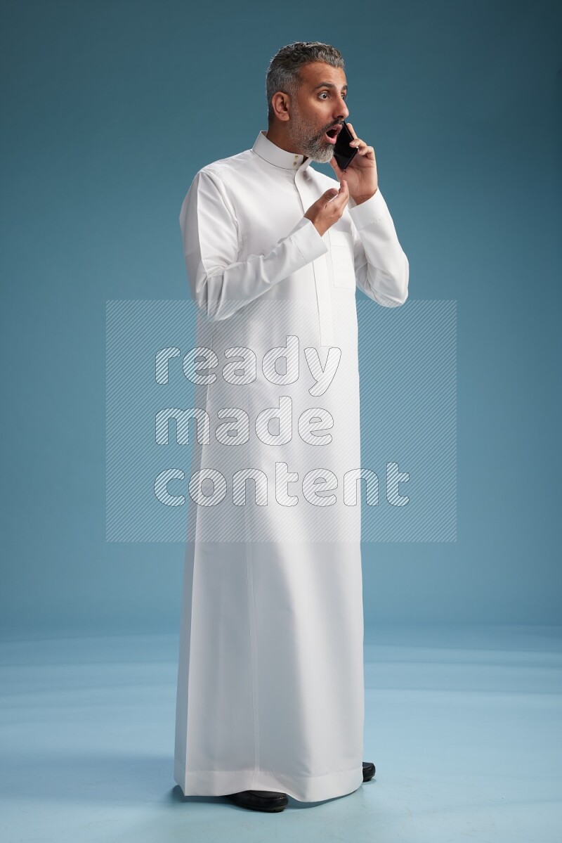 Saudi man wearing thob talking on the phone on blue background