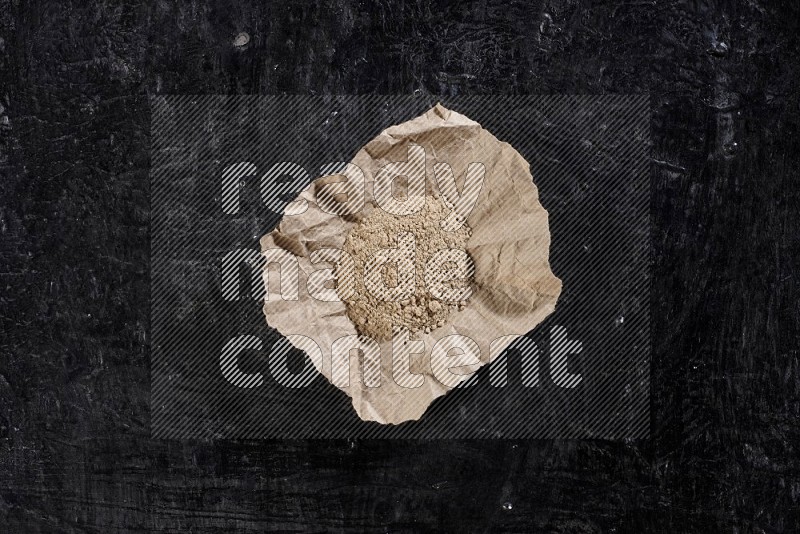 A crumpled piece of paper full of garlic powder on a textured black flooring in different angles