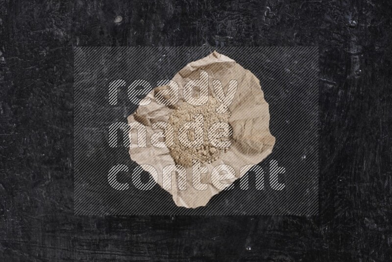 A crumpled piece of paper full of garlic powder placed on a textured black flooring