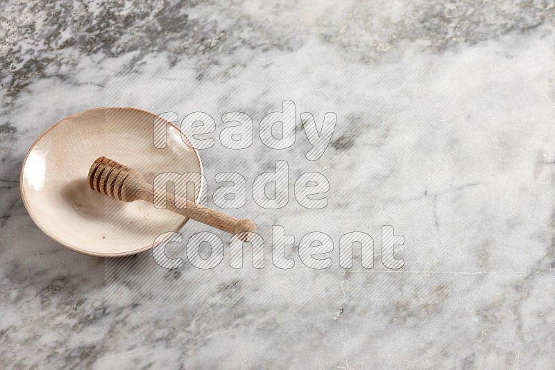 Beige Pottery Plate with wooden honey handle in it, on grey marble flooring, 65 degree angle