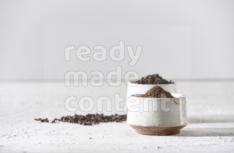 2 Beige ceramic bowls, one full of cloves and the other full of powder on textured white flooring